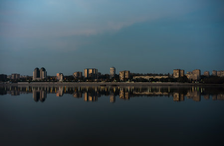 Evening cityscape on the banks of a wide river with tall buildings reflected in itの写真素材