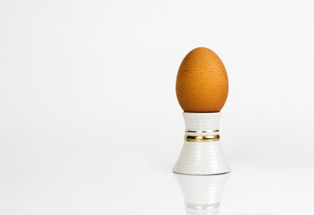 Chicken egg on a stand is peeled on a white background with reflection