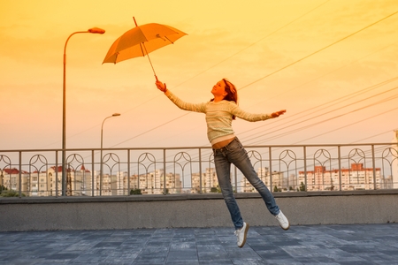 The girl is flying with an umbrella. Tinted with yellow filterの写真素材