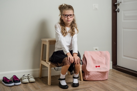 A pretty young schoolgirl with blond hair going to school, sitting next to the doorの写真素材