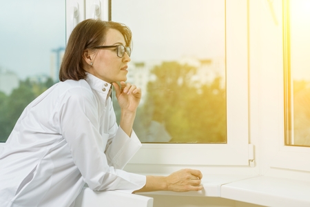 Side view portrait of a female doctor looking out the window in a modern hospital or medical centerの写真素材