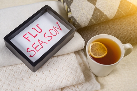 Flu season - text in frame. Background warm woolen clothes, a cup of hot tea.の写真素材