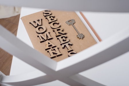 The book is wrapped in old paper and signed with wooden letters woman secrets, on the book key. White background chair in the interior of the house.の写真素材