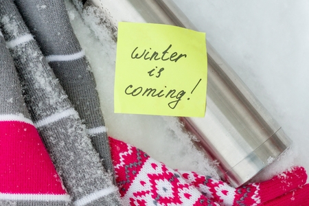 Winter is coming, text on the sticker. Winter background - in the snow a scarf, gloves, thermos.の写真素材