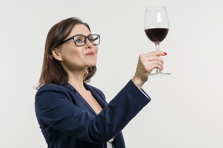 Business woman is holding and looking at a glass of red wine. White studio background.の写真素材