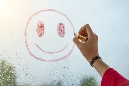 Hand draws a positive funny smiley on a rainy autumn windowの写真素材
