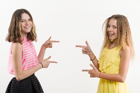 Attractive positive two teenage girls pointing her index finger away, indicating copy space on white blank wall for your content or promotional informationの写真素材