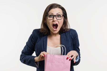 Surprised adult woman looking shopping bag, white background.の写真素材