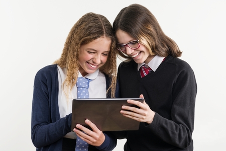 Happy high school friends are teenage girls, look at the tablet and emotionally react, white background, in school uniformの写真素材