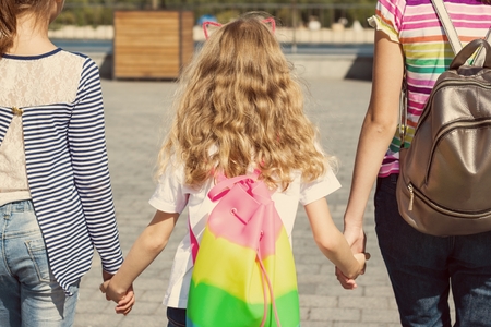Rear view of three girls' children. They hold hands, walk in the city. Background of an urban summerの写真素材