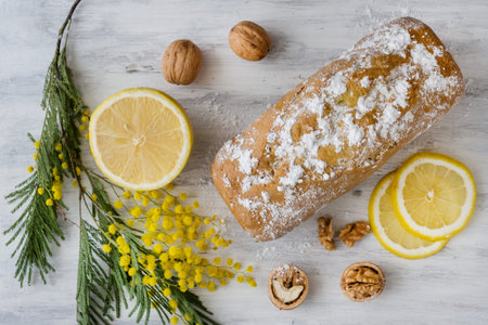 Lemon cake with nuts on a wooden white surface, a twig of mimosa flowers.の写真素材
