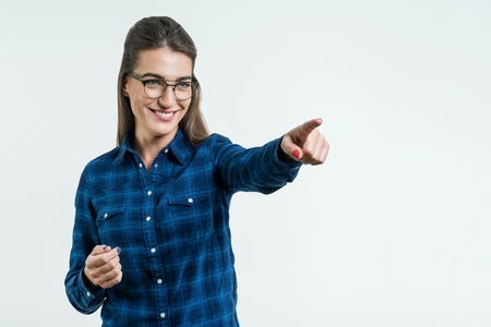 Portrait of young positive girl in glasses smiling winking looking at camera pointing finger in side over white background.の写真素材