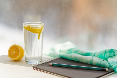 Designer black notebook, glass of mineral water with lemon, window background.の写真素材