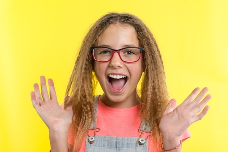 Happy teenage girl blonde with curly hair gesticulating, bright yellow studio backgroundの写真素材