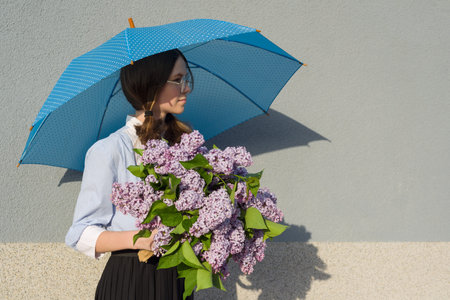 Profile portrait romantic teenage girl with bouquet of lilacs, with an umbrella on gray wall background. Outdoor, copy spaceの写真素材