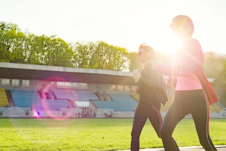 Outdoor sports and fitness family. Sporty mature mother and teen daughter. Woman and girl are running around in the city stadium. Copy spaceの写真素材