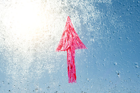 Handwritten red arrow on rainy window. Background drop of water on the glass, blue sky, sun