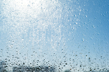 Rain drops on the window. Background blue sunny sky, drops shine in the sun.の写真素材
