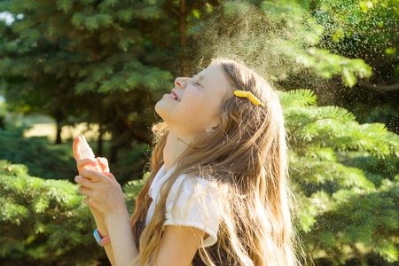 Little girl spraying face with thermal water. Joy and enjoyment on a hot sunny day.の写真素材