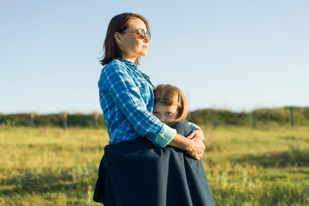 Portrait of parent and child. Mother hugs her little daughter. Nature background, rural landscape, green meadowの写真素材