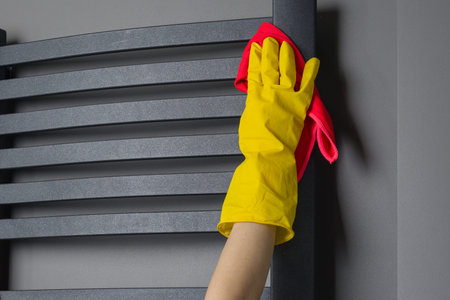 Housemaid woman is cleaning. Wipes the bathroom heater with rag.