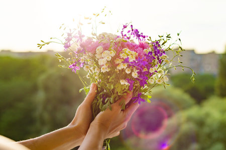 Woman holding bouquet of summer wildflowers in her hands. Background sky, silhouette of the city, sunset.の写真素材