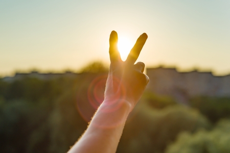 Hand showing two fingers or victory gesture. Background evening sunset, city silhouette.の写真素材