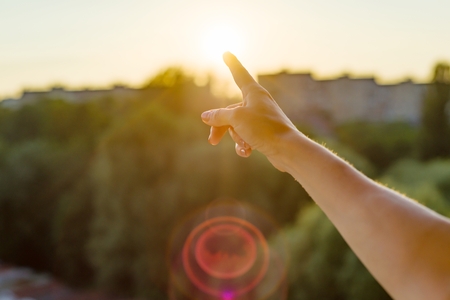 Gesture with the index finger towards the sunset. Background sky, silhouette of the city, sunset.の写真素材