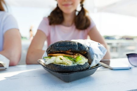 Close-up of black fast food burger. Background girls teenagers, outdoor summer cafeの写真素材