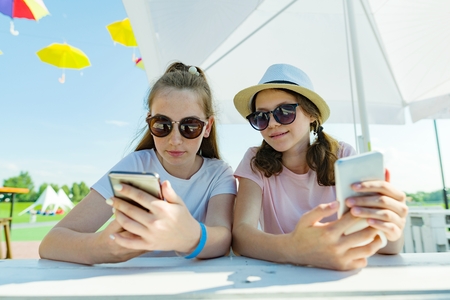 Young teen girls with mobile phones. Sit in a street cafe, sunny summer day in recreation and entertainment areaの写真素材