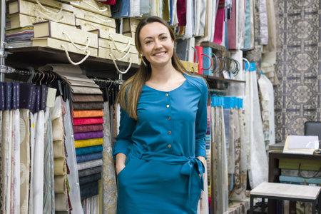 Portrait of happy mature woman owner in interior fabrics store, background fabric samples. Small...