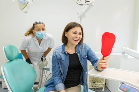 Happy woman patient looking in the mirror at the teeth, sitting in the dental chairの写真素材