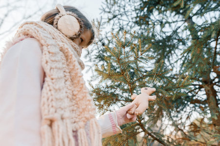 Winter outdoor portrait of child girl near the Christmas tree, smiling girl decorates Christmas tree with toy, golden hour.の写真素材
