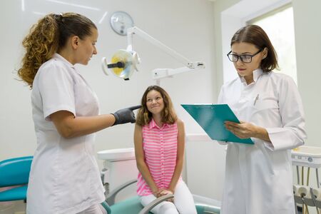 Teenage girl is sitting in a dental chair talking to female dentistsの写真素材