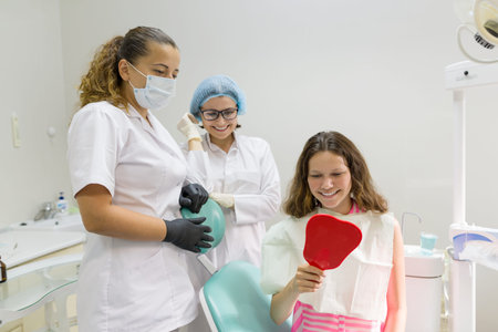 Happy teen girl patient looking in the mirror at the teeth, sitting in the dental chair.の写真素材