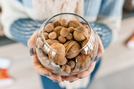 Closeup of glass vase with nuts - hazelnuts and walnuts in hands of woman.の写真素材