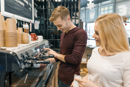 Couple of young male and female coffee shop owners near the counter, talking and smiling, coffee...