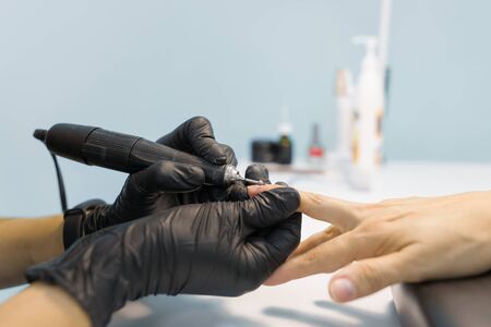 Closeup process of professional manicure. Manicurist woman hands in black gloves making manicure using professional tools. Nail and hand care in beauty salon.の写真素材