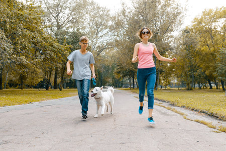 Teenagers running with white dog Husky on the road in the park.