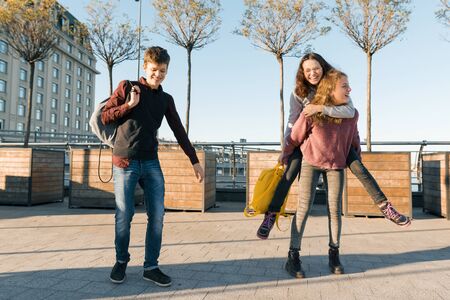 Friends teenagers students with school bags, having fun on the way from school. City background, golden hour.の写真素材