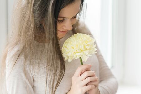 Closeup portrait of girl with large pale yellow flower, young woman with natural make-up smiling, background window. Concept of clear skin, natural herbal cosmetics.の写真素材