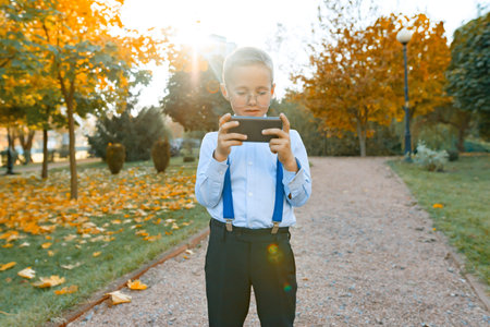 Smart boy in glasses with a mobile phone. A child in a classic shirt in suspenders for trousers,...