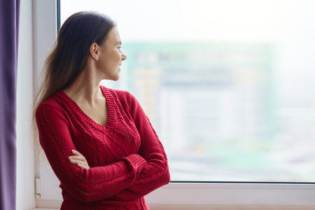 Young smiling confident woman stands near the window, female crossed her arms, woman in a knitted...