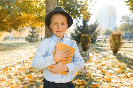 Little boy embraced favorite and beloved book. Background autumn sunny park, golden hour.の写真素材