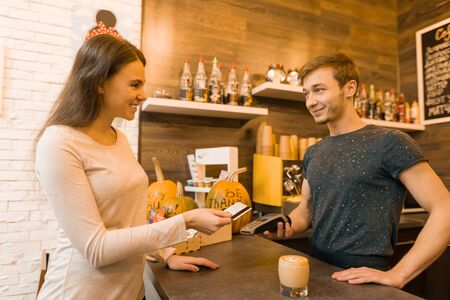 Girl coffee shop client pays coffee by credit card, barista holding a credit card reader machine.