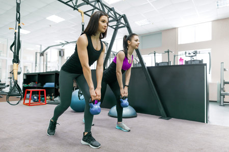 Two young healthy women doing exercises with weight in the gym. Fitness, sport, training, people, healthy lifestyle conceptの写真素材