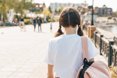 Teenage student girl walking down the street with backpack. Back to school, back view.