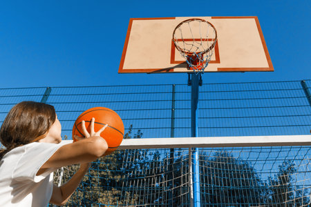 Teenager girl street basketball player with ball on outdoor city basketball court.