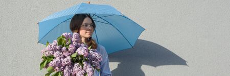 Profile portrait romantic teenage girl with bouquet of lilacs, with umbrella on gray wall background. Outdoor, copy space, panoramic banner.の写真素材