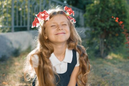 Outdoor portrait of smiling child girl in wreath of pink flowers with eyes closed, girl with blond long wavy hair.の写真素材